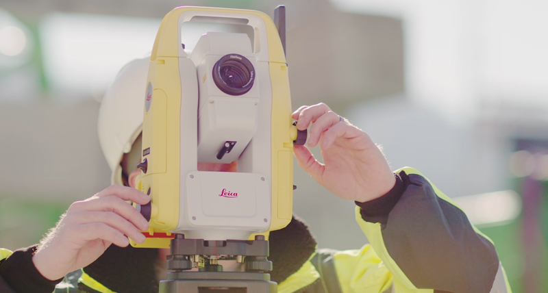 Leica iCON CC80 -maastotallennin ja iCON build -ohjelmisto pisteasettelun kanssa ja rakennusprojekti taustalla.